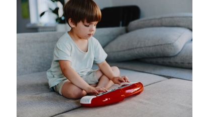 Young boy playing with a toy keyboard in a bright living room, focused and engaged in music, surrounded by soft, cozy furniture.
