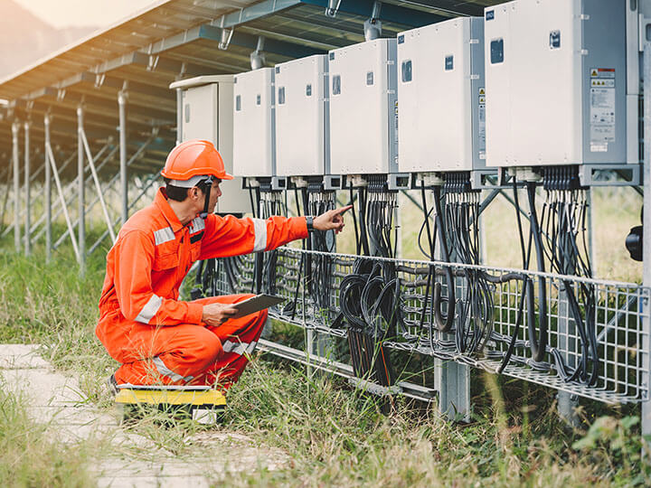 Engineer inspection string of inverters for solar panels with a laptop wearing a orange safety suit and hardhat
